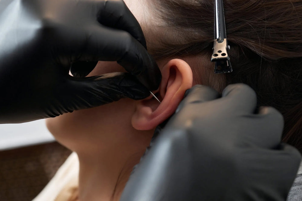 A professional piercing a womens ear, whilst wearing black safety gloves